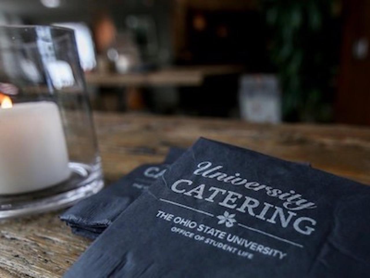 Menu that states University Catering next to a candle holder with a lit candle